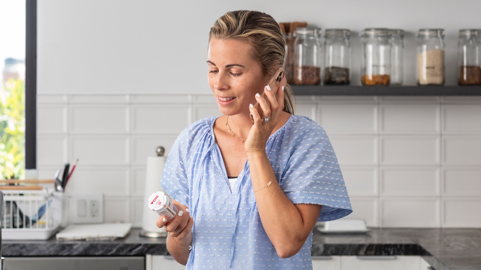 Woman at home talking on phone holding a CVS prescription bottle.